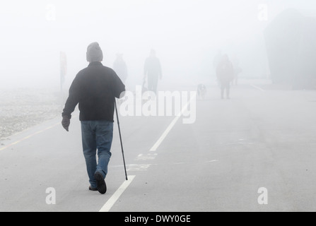 People walking along a promenade in the fog. Stock Photo