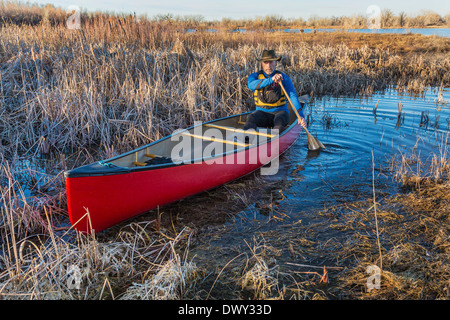 senior male paddling a red canoe through a swamp, early spring Stock Photo