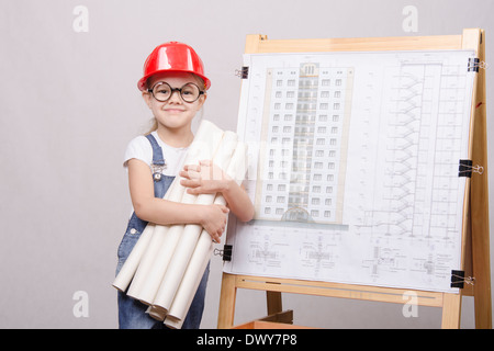 Girl Builder, architect, holding a bunch of drawings, standing at the blackboard with the drawing of the building Stock Photo