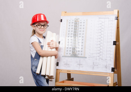 Girl Builder, architect, holding a bunch of drawings, standing at the blackboard with the drawing of the building Stock Photo