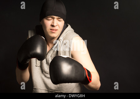 Young boxer grimacing in pain as he stands with his gloved fists raised in the darkness Stock Photo