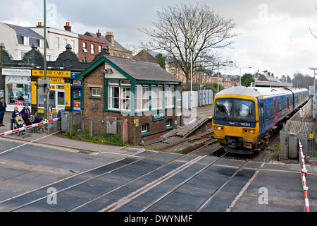 A diesel train leaves Reigate station and prepares to cross the road crossing  and past the signal box Stock Photo