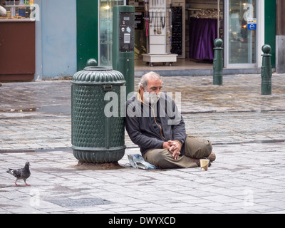 A homeless man sitting on a wet street in Brussels, Belgium. Stock Photo