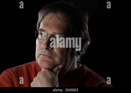 Mature man looks quizzical or thoughtful with his hand on his chin - on black background with dramatic lighting Stock Photo