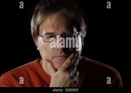 Mature man looks quizzical or thoughtful with his hand on his chin - on black background with dramatic lighting Stock Photo