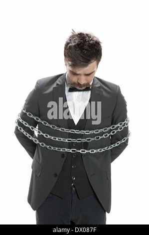 Attractive young man in business suit looks sullen as he stands with chains around him, isolated on white Stock Photo