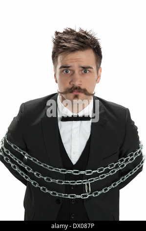 Attractive young man in business suit looks sullen as he stands with chains around him, isolated on white Stock Photo