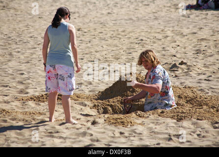 man digging a deep hole in the sand at Bournemouth beach with woman stood watching at Bournemouth, Dorset UK  in March Stock Photo