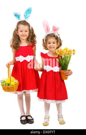 Happy two sisters with bunny ears holding hands and holding basket with easter eggs and daffodils flower isolated on white Stock Photo