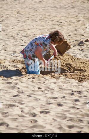 man digging a deep hole in the sand at Bournemouth beach, Bournemouth, Dorset UK in March Stock Photo