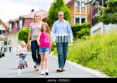 Young family with Mother, father and daughters walking through a housing estate, perhaps they make a trip or excursion Stock Photo