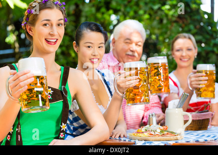 In Beer garden - friends in Tracht, Dirndl and Lederhosen drinking a fresh beer in Bavaria, Germany Stock Photo