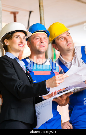 Construction site team or architect and builder or worker with helmets controlling or having discussion of plan or blueprint Stock Photo