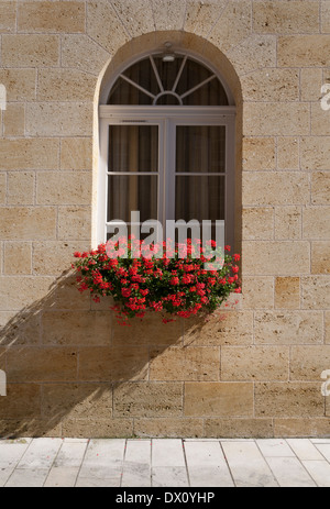 Window and stone wall with red flowers in a window box In Saint Emilion in Bordeaux France Stock Photo