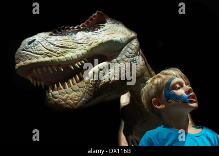 Child blond boy making fun with real life model of Tyrannosaurus rex dinosaur - compared in size with a human child Stock Photo