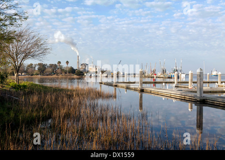 Fluffy white clouds (Altocumulus floccus) reflected in the still waters, trawlers at dock and a power plant in the distance. Stock Photo
