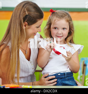 Happy girl doing paper origami with her mother in nursery Stock Photo