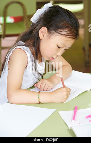 Chinese girl learning to write in kindergarten with a pen at a table Stock Photo