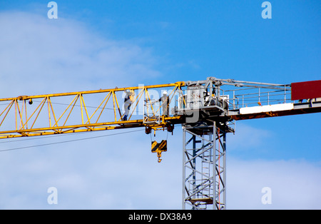 Yellow tower crane and workers against blue cloudy sky Stock Photo