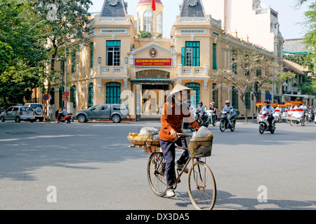 Woman cyclist with traditional Asian hat often referred to as a coolie hat cycles through Hanoi Stock Photo