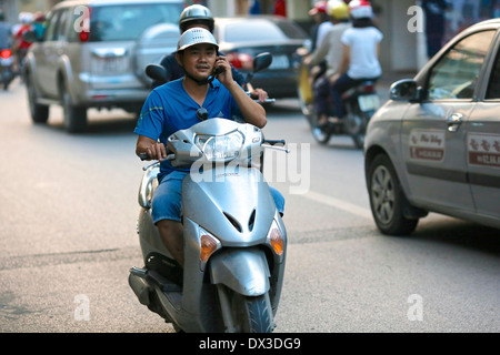 A young man uses a mobile phone whilst riding a scooter through the Old Quarter in Hanoi. Hanoi, Vietnam, Southeast Asia Stock Photo