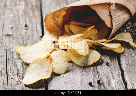 Paper cornet with potato chips with salt and pepper over old wooden table. See series Stock Photo