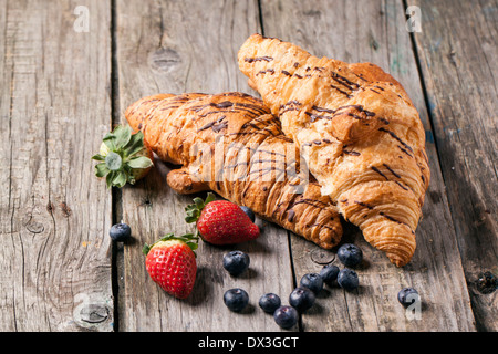 Two fresh croissant with berries over old wooden table. Stock Photo