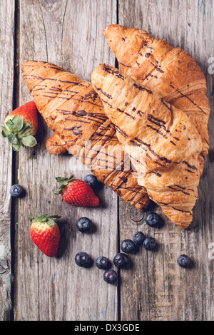 Top view on two fresh croissant with berries over old wooden table. Stock Photo