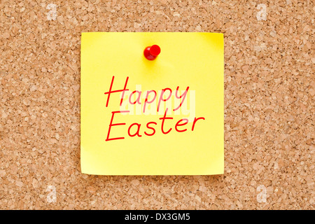 Happy Easter written on an yellow sticky note pinned on cork bulletin board. Stock Photo