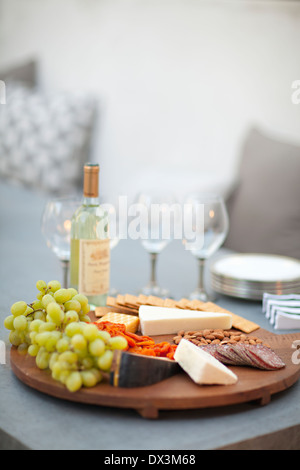 Cheese, crackers, nuts, grapes and salami on wooden cheeseboard next to white wine, tilt Stock Photo