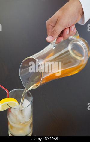 Man's hand pouring iced tea from pitcher into glass with lemon wedge on black background, high angle view, close up Stock Photo