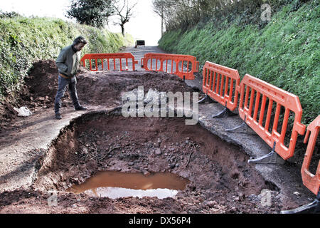 Sandford, Crediton, Devon, UK. 18th March 2014. A monster pothole has closed a busy lane between Crediton and Sandford in Devon following the recent storms.  Preparatory work has taken place to ascertain the extent of the damage, and the cost of repairing the road is being estimated at £7000. It is unknown when the repairs will take place, and the closure is affecting local farmers as well as local schoolchildren who now have a much longer route to school. Credit nidpor/ Alamy Live News Stock Photo