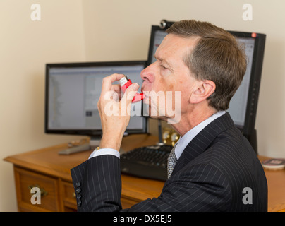 Businessman sitting at desk with computer screens using asthma inhaler Stock Photo