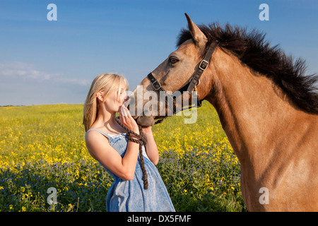 Portrait of a young girl kissing her brown horse out in a yellow rapeseed field Stock Photo