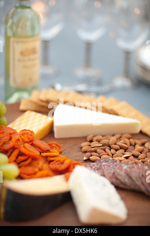 Cheese, crackers, nuts, grapes and salami on wooden cheeseboard next to white wine, close up Stock Photo