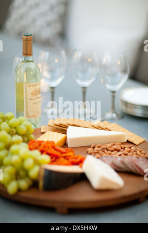 Cheese, crackers, nuts, grapes and salami on wooden cheeseboard next to white wine, close up Stock Photo