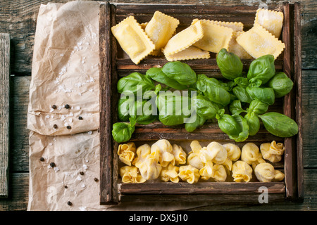 Top view on wooden box with homemade pasta ravioli and perle with fresh basil on old wooden table. Stock Photo