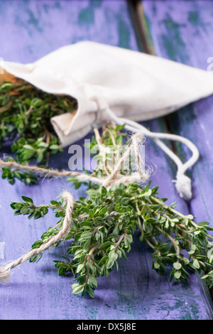 Bunch of fresh thyme and thyme in textile bag on violet wooden table Stock Photo