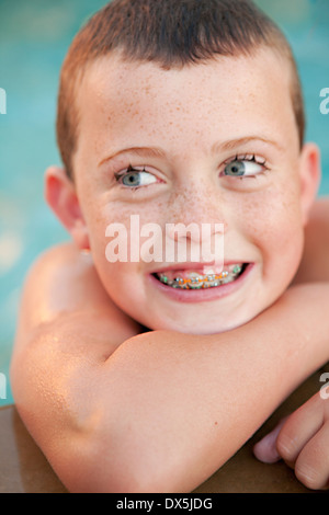 Blue eyed boy with braces and freckles in swimming pool, toothy smile, close up