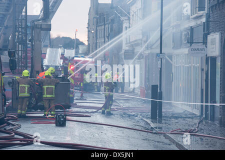 Firefighters by engines & burning building, tackle fire with water jets from hoses, aimed at burnt-out, blackened windows - Harrogate, Yorkshire, England, UK. Stock Photo