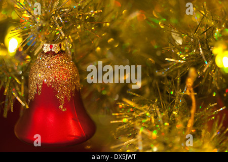 Red bell ornament hanging on illuminated Christmas tree, close up Stock Photo