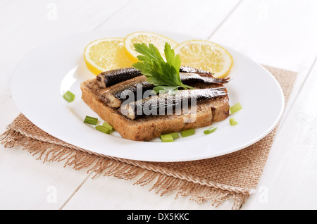 Sprats sandwiches on white plate on wooden table Stock Photo