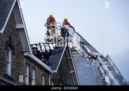 Brave firefighter crew (2 firefighters) up high ladder on platform, inspecting fire damage to roof of town centre building - Harrogate, North Yorkshire, England, UK. Stock Photo