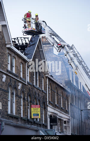 Brave firefighter crew (2 firefighters) up high ladder on platform, inspecting fire damage to roof of town centre building - Harrogate, North Yorkshire, England, UK. Stock Photo