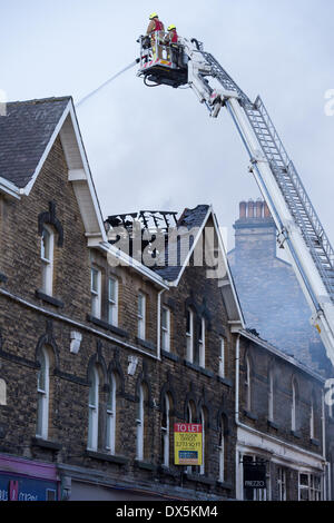 Brave firefighter crew (2 firefighters) up high ladder, tackle fire with water hose at town centre building - Harrogate, North Yorkshire, England, UK. Stock Photo