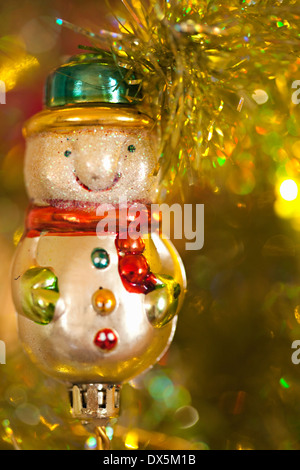 Snowman ornament hanging on illuminated Christmas tree, close up Stock Photo