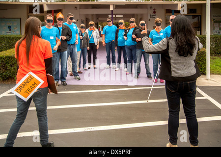 Visitors to a school for the blind in Tustin, CA, are blindfolded to allow them to experience sightlessness as they learn to use a white cane for walking in a parking lot. Note team sign. Stock Photo