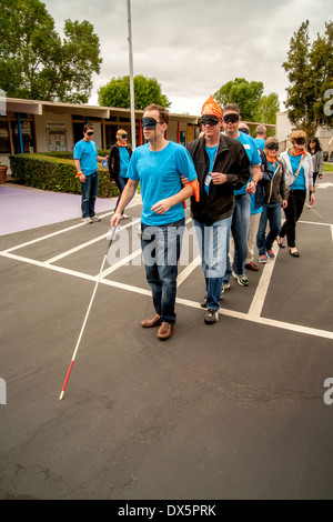 Visitors to a school for the blind in Tustin, CA, are blindfolded to allow them to experience sightlessness as they learn to use a white cane for walking in a parking lot. Stock Photo