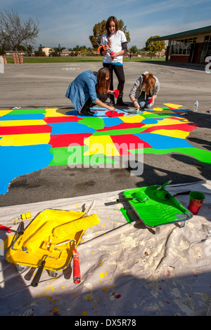 Young adult volunteer artists paint a map of the United States on an elementary school playground in Garden Grove, CA. Note paint rollers and trays. Stock Photo