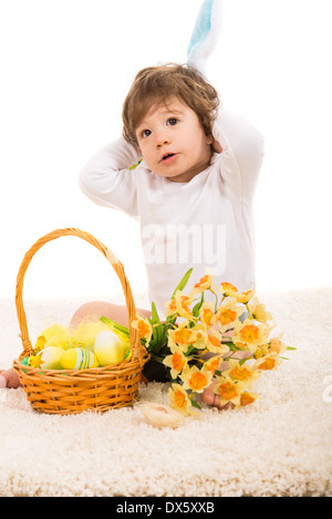 Lovely bunny toddler boy with Easter basket and flower looking away Stock Photo